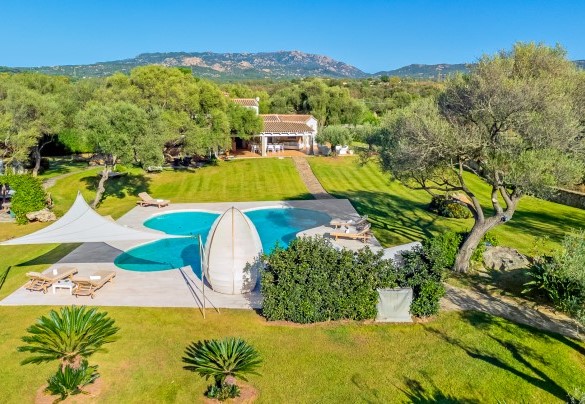 Panoramica aerea  della piscina e della villa totalmente immersa in un rigoglioso prato incorniciata dal massiccio della Cugnana – Villa Typha