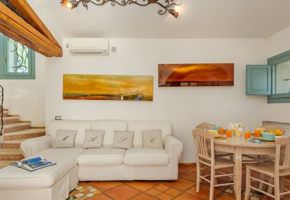 Luminoso open space con vetrate che si affacciano sulla veranda e sul giardino in cui troviamo la zona living con divano e tavolo rotondo – Villa Typha